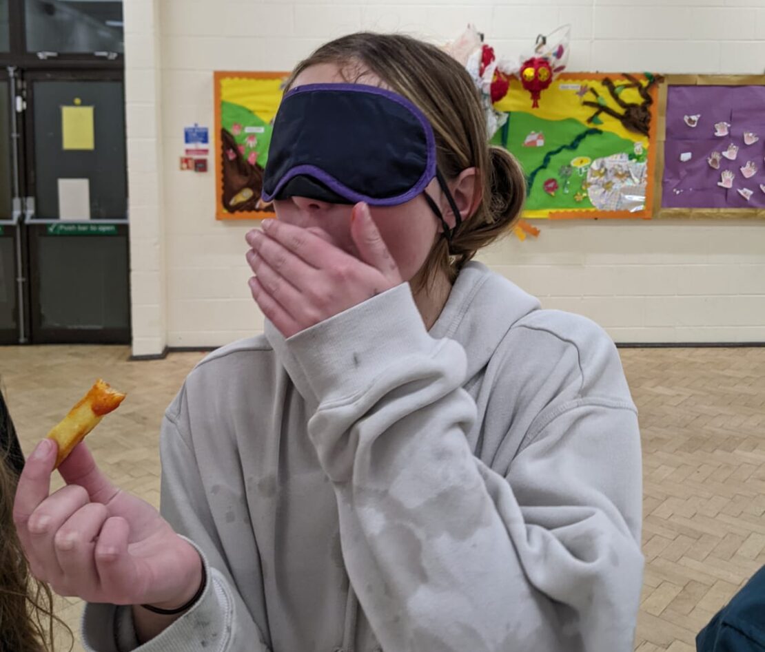 A blindfolded Scout tries to identify the normal or spicy ketchup she has just dunked her chip into.
