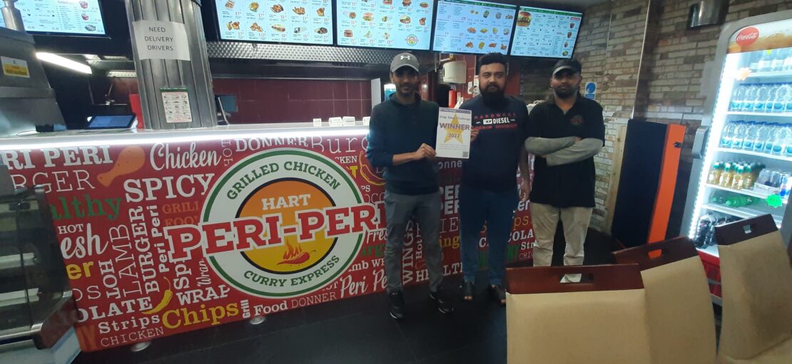 Three staff members of Hart Peri-Peri fast food restaurant standing in front of the serving counter, proudly holding our chip shop challenge certificate.